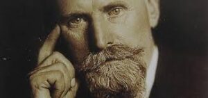 Retrato en primer plano de un hombre de barba prominente y mirada intensa, con un fondo neutro que resalta sus rasgos.