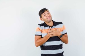 Hombre joven con camiseta de rayas, sonriendo y haciendo un gesto de gratitud o alegría, fondo blanco.