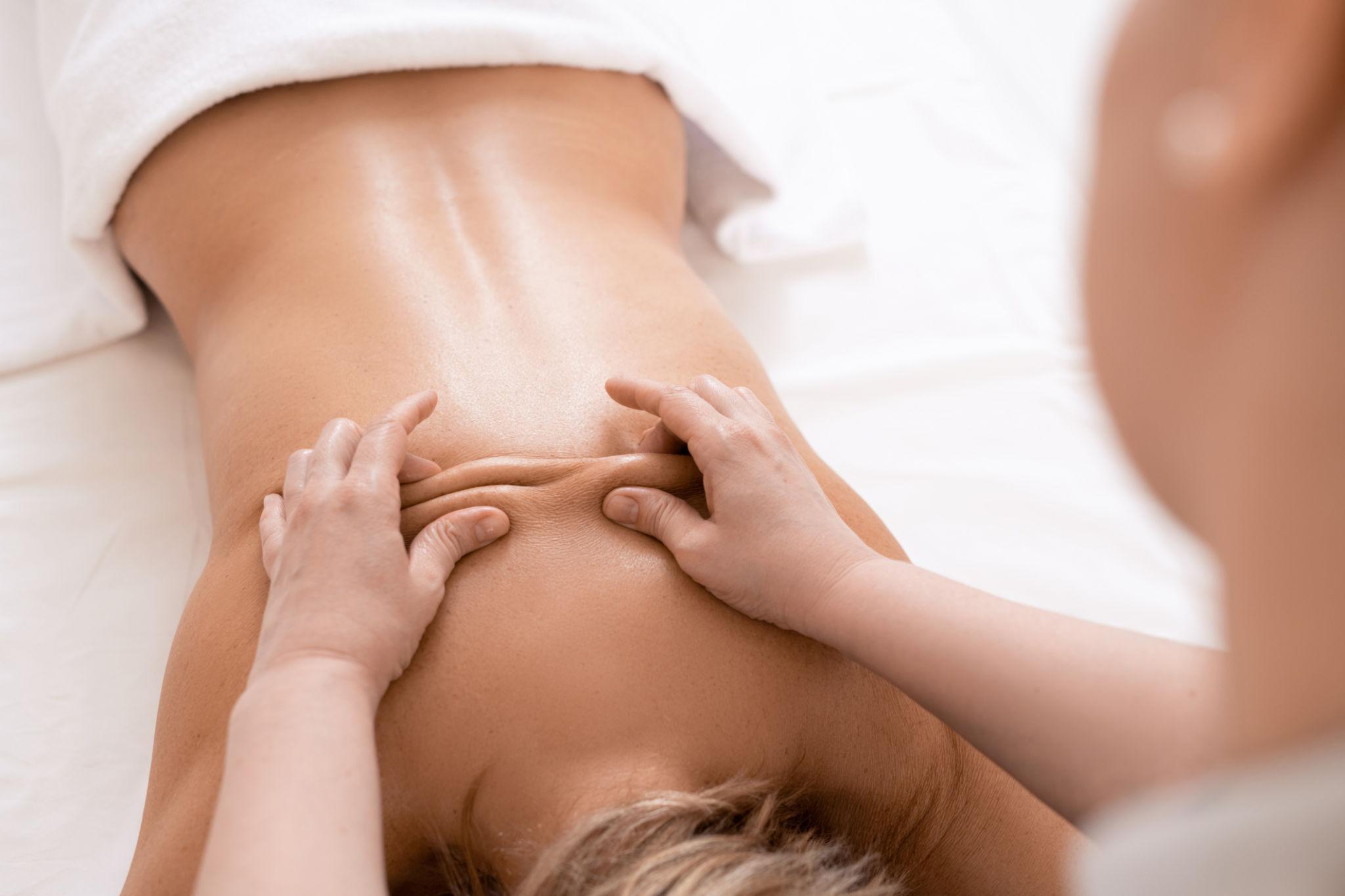 Mujer recibiendo un masaje en la espalda, con manos aplicando presión en la piel, en un ambiente relajante. Ideal para promover la terapia de masajes y el bienestar físico.